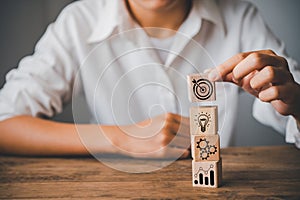 Hand holding a wooden block with icons about business strategy and action plan to lead the goal of business success.Business