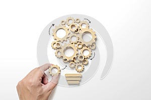 Hand holding wooden cog flowing process management lightbulb shape on white background