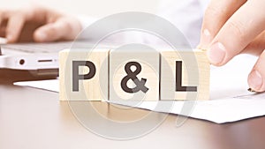 hand holding wooden cube with P and L text on table background. financial, marketing and business concepts