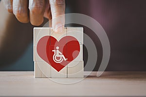 Hand holding wooden cubes with disabled people in red heart symbols,  aged senior nurse care, disabilities health care