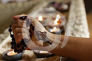 .Hand holding wooden rosary beads tightly with Jesus Christ holy cross crucifix on candle lights background/