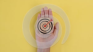 A hand holding a wooden target with a red arrow pointing to the center