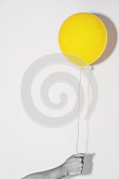 Hand holding yellow balloon on white wall