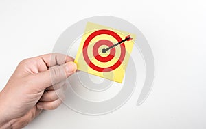 Hand holding yellow paper sticky note with target, goal, aim. set up business objective target and success and business goals