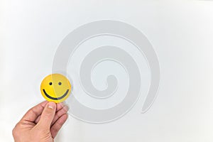 A hand holding a yellow smiley face on a white background. Happy customer, positive feedback and good service concepts