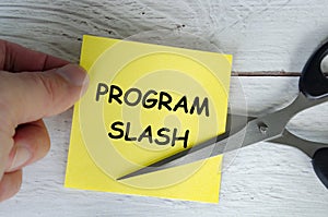 Hand holding a yellow sticky note with the words Program Slash written on it, while a pair of scissors is cutting through the note
