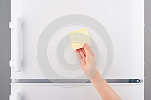 Hand holding yellow sticky paper note on white refrigerator