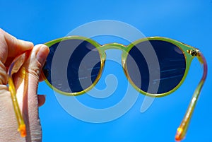 Hand Holding Yellow Sun Glasses over Blue Summer Sky Copy Sapce for Text