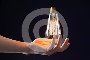 hand holds in the air a burning vintage light bulb