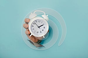 Hand holds alarm clock through a blue paper hole. Time management and deadline concept