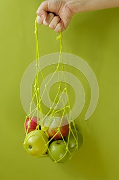 Hand holds a bag of string bag with ripe apples on a green background. Eco-friendly packaging. Reusable