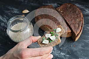 Hand holds bitten sandwich artisan bread with onion chives and garlic, glass jar with sourdough, cuts loaf rye bread