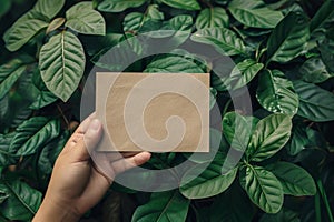 Hand holds blank brown paper card on green leaves background. Generative AI