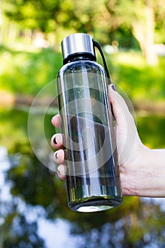 Hand holds bottle of water on lake and trees background