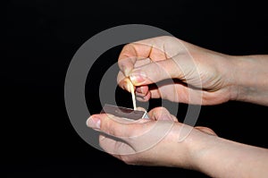 A hand holds a burning match on a black background. A wooden match burns in the hands of a macro. Igniting a match on a box. Smoke