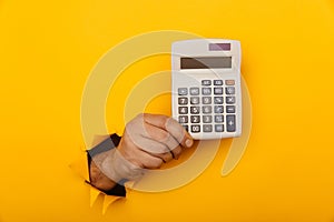 Hand holds calculator through a paper hole in yellow background