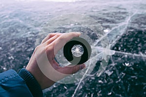 Hand holds the camera lens on the background of the frozen Lake