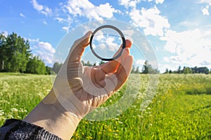 Hand holds a circular polarizer filter on field background.