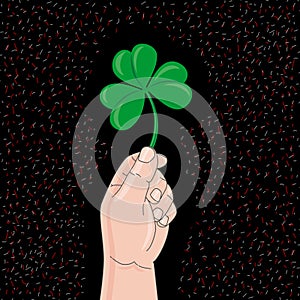 Hand holds clover on black background. St. Patrick Day Symbol