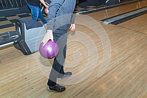 A hand holds a colored bowling ball. Wooden walkway in a bowling alley. Game with balls. A male hand throws a ball onto a track.