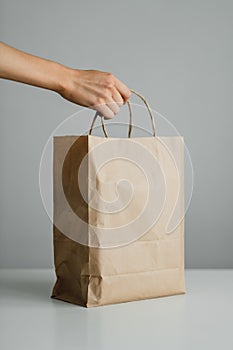 Hand holds craft eco pack on gray background, mock up. Delivery concept