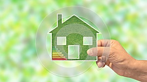 Hand holds an eco green house, with energy efficiency rating.