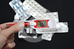 Hand holds an electronic thermometer on the background of pills