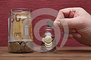 Hand holds euro coins and bill on the burgundy red background in a money box
