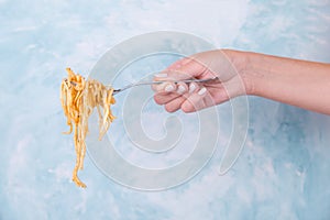 The hand holds a fork with the noodles hanging down, the appetite spaghetti with the sauce on a blue background