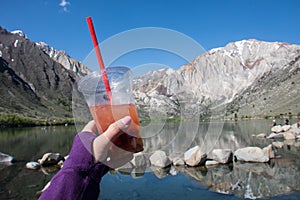 Hand holds a fruity tea drink placed in front of Convict Lake located off of US-395, near Mammoth Lakes California in the eastern