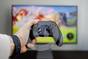 A hand holds a game controller in front of the monitor