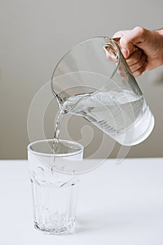 The hand holds a glass jug of water and pours into a transparent glass