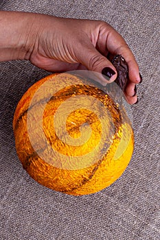 A hand holds a homemade orange papier-mache pumpkin for Halloween on a burlap background