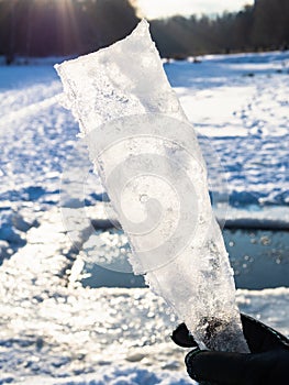 Hand holds ice block illuminated by sun in winter