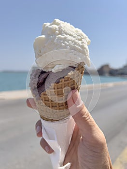 hand holds ice cream cone over sea in a sunny day