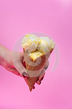A hand holds an ice cream cone on a pink popsicle background in a waffle cup.