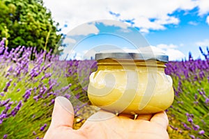 Hand holds jar with honey against lavender flowers