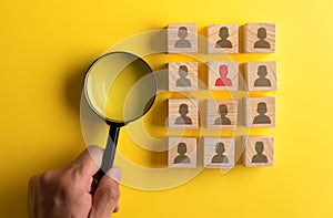 Hand holds a magnifying glass over wooden blocks with human silhouettes isolated on yellow background