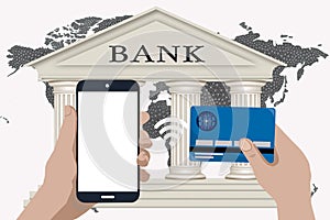 Hand holds mobile phone and credit card on white with world map and bank in the background. Contactless payment concept