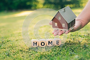 A hand holds a model house above a meadow.