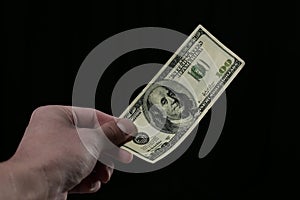 Hand holds one hundred dollar bill on black background