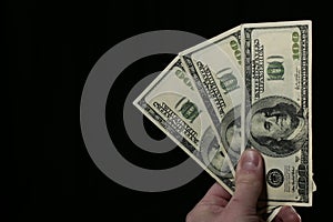 Hand holds one hundred dollar bills on black background
