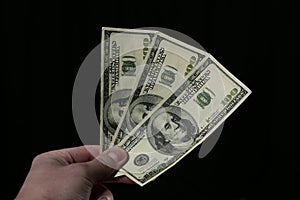 Hand holds one hundred dollar bills on black background