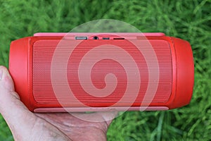 a hand holds one red small mobile music electronic speaker