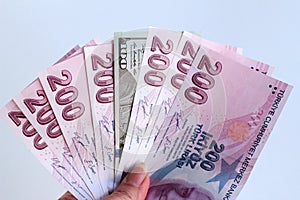 Hand holds one thousand four hundred Turkish lira and only one hundred American dollars on a white