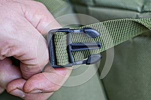 Hand holds open black plastic carabiner on the green harness