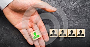 A hand holds out a green leader figure to a team of employees. Headhunter recruits staff and business personnel management photo