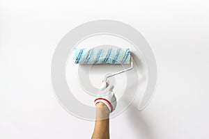 Hand holds paint roller and painting a White wall. Decorator`s hand painting wall with roller