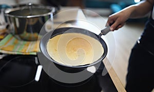 Hand holds pan with pancake, cooking at home