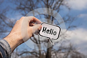 A hand holds a paper cloud with the word hello on the background of trees